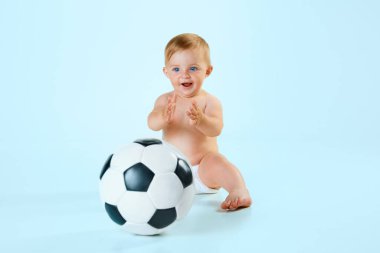 Mutlu, gülümseyen küçük bebek, bebek bezli çocuk açık mavi stüdyo arka planında futbol topuyla oynuyor. Çocukluk kavramı, yeni doğmuş yaşam tarzı, mutluluk, bakım. İlan için alanı kopyala