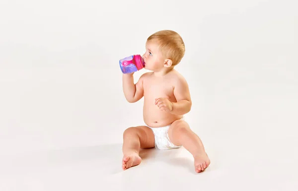かわいい かわいい赤ちゃん おむつに座って食べるトッドラー ホワイトスタジオの背景からボトルから水を飲む 子供の頃の概念 新生児のライフスタイル Adのためのスペースをコピーする — ストック写真