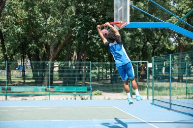 Genç bir adamın dinamik görüntüsü, hareket halindeki basketbolcu, potaya top atıyor. Açık hava eğitimi. Profesyonel spor, rekabet, hobi, oyun, aktif yaşam tarzı kavramı