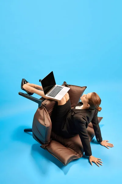 认真的女商人 坐在倒下来的椅子上 跪在笔记本电脑上在蓝色工作室的背景下工作 业务概念 日常工作 截止日期 自由应聘人员 办公室 — 图库照片