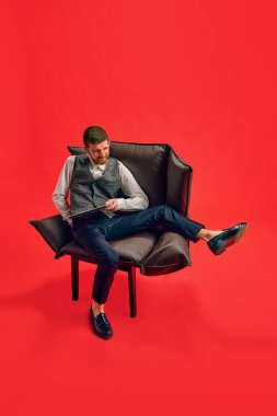 İşadamı, çalışan kırmızı stüdyo arka planına karşı çalışmak için koltukta rahat bir pozisyon bulamıyor. İş anlayışı, çalışma alışkanlığı, teslim tarihi, serbest çalışma, ofis, reklam