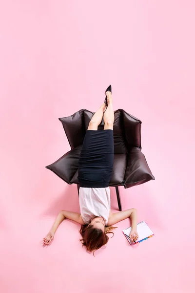 女商人不舒服地躺在扶手椅上 一边工作 一边在粉红的工作室背景下做笔记 业务概念 日常工作 截止日期 自由应聘人员 办公室 — 图库照片