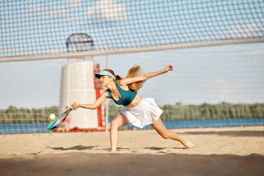 Rekabetçi kadın, atlet, maç sırasında hareket eden profesyonel tenisçi raketle topa vurmak, yaz günü plajda antrenman yapmak. Spor anlayışı, boş zaman, aktif yaşam tarzı, hobi, reklam