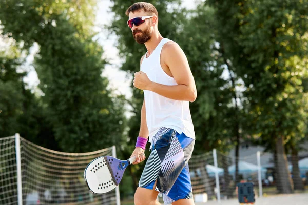 stock image Bearded man in sunglasses going on beach to play paddle tennis on warm summer day. Outdoor activity. Concept of sport, leisure time, active lifestyle, hobby, game, summertime, ad