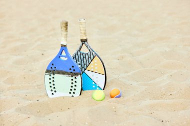 Tenis raketi ve toplar kumda yatıyor. Yaz oyunu, sıcak açık hava eğitimi. Spor malzemeleri. Spor anlayışı, boş zaman, aktif yaşam tarzı, hobi, oyun, yaz zamanı, reklam