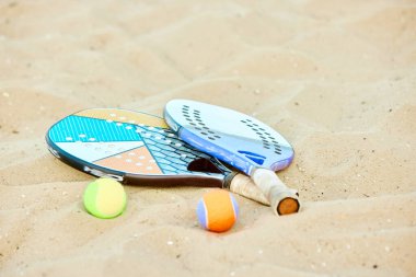 Tenis raketi ve toplar kumda yatıyor. Yaz oyunu, sıcak açık hava eğitimi. Spor malzemeleri. Spor anlayışı, boş zaman, aktif yaşam tarzı, hobi, oyun, yaz zamanı, reklam
