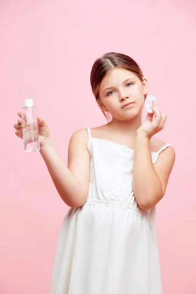 かわいい少女の肖像画 ピンクのスタジオの背景に顔のトナーを塗った白いドレスの子供 スキンケア 幼少期 化粧品 オーガニック製品 広告のコンセプト — ストック写真