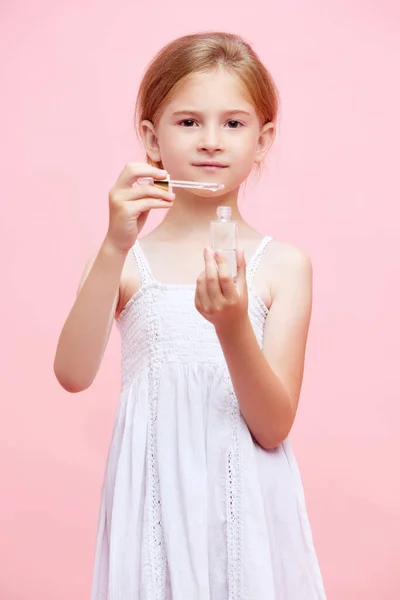 小さい女の子 顔の血清を適用する子供は ピンクのスタジオの背景に対して皮膚の世話をする スキンケア 幼少期 子供の化粧品と健康 有機製品 広告のコンセプト — ストック写真