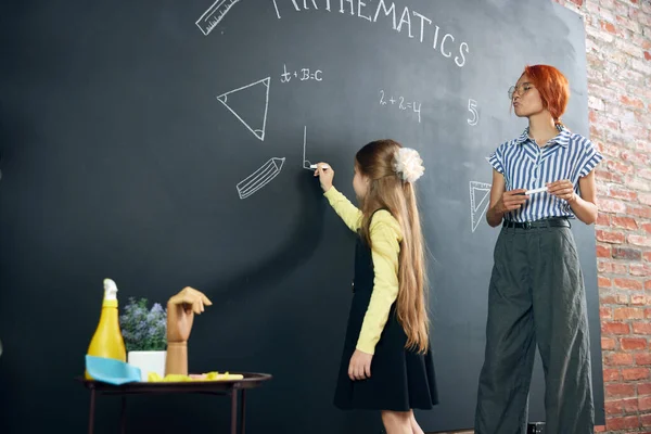 聪明的小女孩和老师一起站在黑板旁边 写和解题 在学校上几何课 生活方式的概念 — 图库照片