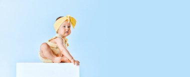 Şirin, güzel küçük kız bebek, sevimli sarı kıyafetler giyen bebek, sakince mavi stüdyo arka planında oturuyor. Çocukluk kavramı, aile, mutluluk, bakım. Reklam için boşluk kopyala. Pankart