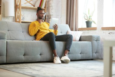 Genç bir Afrikalı, evdeki kanepede oturuyor ve Ablett aracılığıyla internet üzerinden iş görüşmesi yapıyor, iş arkadaşlarıyla görüşüyor. İş ve eğitim kavramı, serbest meslek, modern yaşam tarzı