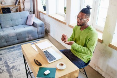 Genç Afrikalı bir adam evde masada oturuyor ve iş arkadaşlarıyla dizüstü bilgisayarla video görüşmeleri yapıyor, projeleri tartışıyorlar. İş ve eğitim kavramı, serbest meslek, modern yaşam tarzı