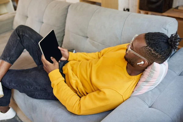 Junger Afrikaner Liegt Auf Dem Sofa Und Hört Über Kopfhörer — Stockfoto