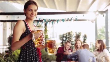 Güzel, gülümseyen, genç bir kadın, bardaki arkadaşlara bira ve bira servisi yapan büyük bardaklar. Oktoberfest, geleneksel zevk, arkadaşlık, boş zaman, eğlence konsepti