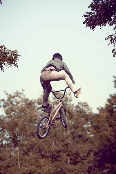 バックビュー ヘルメットに乗っている若者のダイナミックなイメージ Bmx 自転車の森で トレーニング 困難で危険なトリックを行います アクティブライフスタイル スポーツ 極端なダイナミクス フリースタイルの概念 — ストック写真