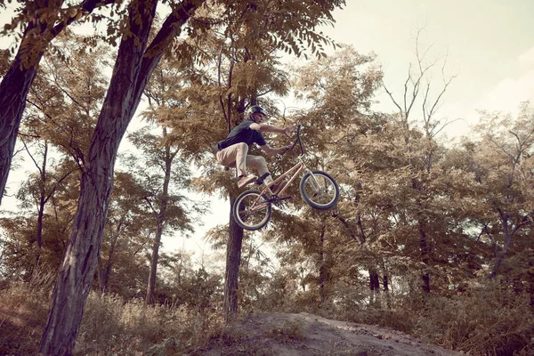 森の外でヘルメットのトレーニングをしている若者 バイクに乗ってトリックをする 秋の乗り物 極端な男 アクティブライフスタイル スポーツ 極端なダイナミクス フリースタイルの概念 — ストック写真