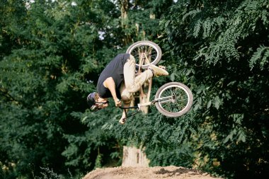 Yaz etkinliği. Ormanda BMX bisikleti süren genç bir adam tehlikeli ve zor numaralar yapıyor, bisikletle atlıyor. Aktif yaşam tarzı, spor, ekstrem, dinamik, hobi, serbest stil kavramı