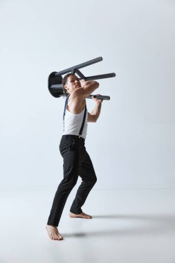 Kaslı vücutlu, gri stüdyo arka planına karşı sandalyeyle poz veren yakışıklı olgun bir adamın portresi. Duygular. Erkeklerin güzellik anlayışı, vücut bakımı, moda, sağlık, sağlıklı yaşam tarzı, reklam