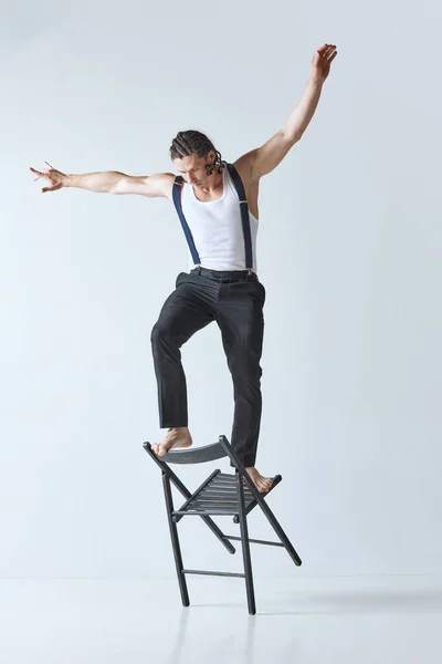 Keep life balance. Portrait of handsome mature man with muscular body posing on chair against grey studio background. Concept of mens beauty, body care, fashion, wellness, healthy lifestyle, ad