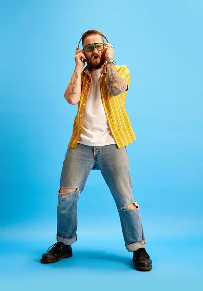 스튜디오 배경에 헤드폰에서 음악을 노란색 셔츠와 선글라스에 감정적인 수염된 남자의 — 스톡 사진