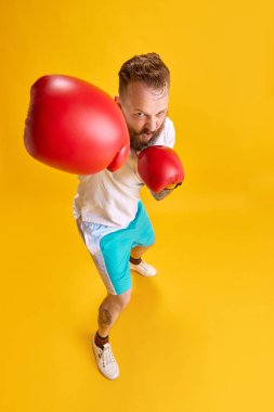 Sakallı, duygusal bir adam spor giyim ve parlak sarı arka planda boks eldivenleri. Yumruk. Üst Manzara. Spor anlayışı, güç, moda, mim duyguları, yaşam tarzı, reklam