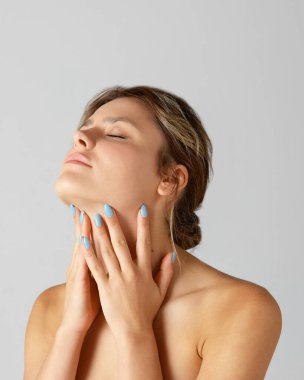 Cildine özen gösteren narin, genç ve güzel bir kadın. Gri arka planda boyuna dokunuyor. Çıplak omuzlu bir model. Doğal güzellik kavramı, kozmetik ve dermatoloji, cilt bakımı, kozmetik, reklam.