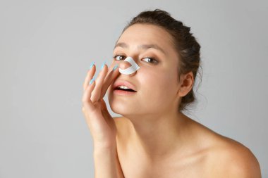 Gri stüdyo geçmişine karşı burun üstüne burun bandı takan genç ve güzel bir kadın. Güzellik, kozmetoloji ve dermatoloji kavramı, estetik cerrahi, cilt bakımı, reklam.