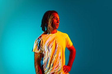 Korkulu genç Afrikalı bir adamın portresi neon ışıkta mavi, cyan arka planda duruyor. Vücutta ışık yansıması. Sanat, moda, modern tarz, siber punk, fütürizm, reklam