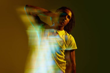 Neon ışıkta yeşil arka planda poz veren şık Afrikalı genç bir adam. Karışık ışık efekti. Hologram. Sanat, moda, modern tarz, siber punk, fütürizm, reklam