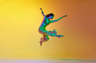 Genç bir kadın, modern profesyonel dansçı, şık kıyafetler içinde, parlak ışık altında sarı arkaplan üzerinde. Modern dans stili kavramı, hobi, sanat, performans, yaşam tarzı, reklam
