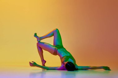Esnek, atletik genç bir kadın iç çamaşırlarıyla neon ışıkta sarı renkli arka planda dans ediyor. Modern dans stili kavramı, hobi, sanat, performans, yaşam tarzı, reklam