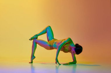Esnek, atletik genç bir kadın iç çamaşırlarıyla neon ışıkta sarı renkli arka planda dans ediyor. Modern dans stili kavramı, hobi, sanat, performans, yaşam tarzı, reklam
