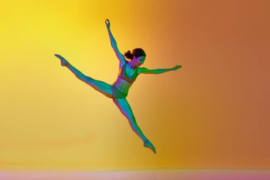 İp duruşu. Genç yetenekli bir kadın, profesyonel dansçı, neon ışıkta sarı renkli arka planda dans ediyor. Modern dans stili kavramı, hobi, sanat, performans, yaşam tarzı, reklam