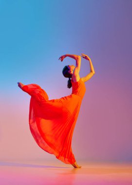 Kırmızı elbiseyle dans eden zarif, zarif genç bir kadın. Neon ışıkta, rengarenk arka planda dans ediyor. Modern dans stili kavramı, hobi, sanat, performans, yaşam tarzı, reklam