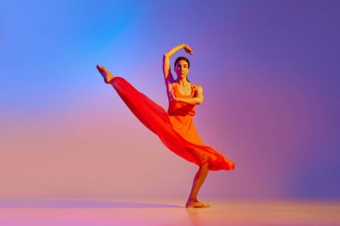 Genç, yetenekli, zarif kırmızı elbiseli bir kadının, neon ışıkta rengarenk arka planda dans edişinin dinamik görüntüsü. Modern dans stili kavramı, hobi, sanat, performans, yaşam tarzı, reklam