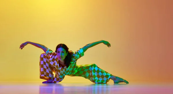 Elegant young woman, professional dancer in motion, dancing contemp against gradient yellow orange background in neon light. Concept of modern dance style, hobby, art, performance, lifestyle, ad
