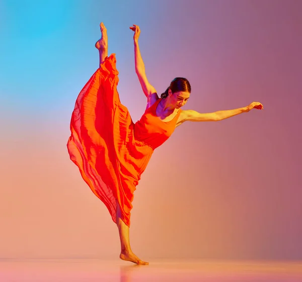 Full-length portrait of young artistic woman in red dress dancing contemp against gradient multicolor background in neon light. Concept of modern dance style, hobby, art, performance, lifestyle, ad