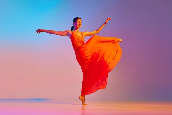 Full-length portrait of young artistic woman in red dress dancing contemp against gradient multicolor background in neon light. Concept of modern dance style, hobby, art, performance, lifestyle, ad