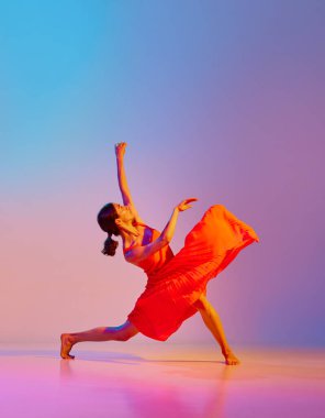 Zarif kırmızı elbiseyle neon ışıkta rengarenk arka planda dans eden sanatsal genç bir kadının dinamik görüntüsü. Modern dans stili kavramı, hobi, sanat, performans, yaşam tarzı, reklam