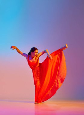 Zarafet ve şefkat. Uzun ve zarif elbiseli genç bir kadın neon ışıkta arka planda çok renkli bir renge karşı dans ediyor. Modern dans stili kavramı, hobi, sanat, performans, yaşam tarzı, reklam