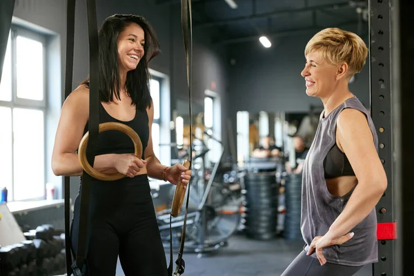 stock image Cheerful middle-aged woman standing in gym, talking with positive fitness trainer. Creating fitness programme, exercises. Concept of active, sportive and healthy lifestyle, fitness, body care, ad