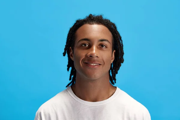若いアフリカ人男性の肖像画 カメラを見て青いスタジオの背景に微笑んでいる白いTシャツの夢を持つ学生 人間の感情 ライフスタイル ファッション 広告の概念 — ストック写真