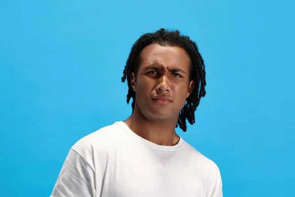 どうしたの 青いスタジオの背景に誤解を抱く白いTシャツの夢を持つ若いアフリカ人男性の肖像画 人間の感情 ライフスタイル ファッション 広告の概念 — ストック写真