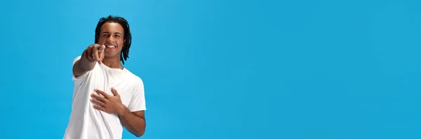 身穿白色T恤 面带微笑的年轻非洲男子指着相机 在蓝色背景下微笑 青春的概念 生活方式 面部表情 班纳广告的复制空间 — 图库照片