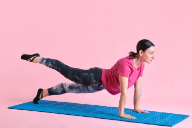 Sportif, sağlıklı, olgun bir kadın, pembe stüdyo geçmişine karşı fitness eğitimi alıyor. Güçlü eller, basın. Spor anlayışı, sağlıklı yaşam tarzı, fitness, vücut bakımı, sağlık, reklam