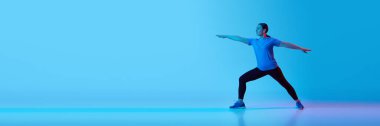 Dinamik duruş. Siyah elbiseli olgun bir kadın, mavi arka planda neon ışıkta esniyor. Spor anlayışı, sağlıklı yaşam tarzı, fitness, vücut bakımı, sağlık. Pankart. İlan için alanı kopyala