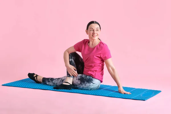 フィットネスマットに座っている笑顔 美しい シニアの女性 トレーニング ピンクのスタジオの背景に対して体を伸ばします スポーツ 健康的なライフスタイル フィットネス ボディケア ウェルネス — ストック写真