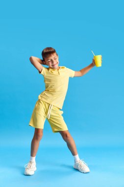 Uzun boylu, neşeli küçük bir çocuk, günlük kıyafetlerle poz veren bir çocuk, mavi stüdyo arka planında dans ediyor. Çocukluk kavramı, çocuk duyguları, tatil, yaz, eğlence ve neşe, reklam