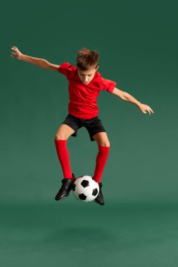 Geleceğin futbolcusu. Küçük bir çocuk, spor giyimli bir çocuk, yeşil stüdyo geçmişiyle top oynuyor. Çocukluk kavramı, çocuk duyguları, spor yaşam tarzı, aksiyon, hobi, reklam