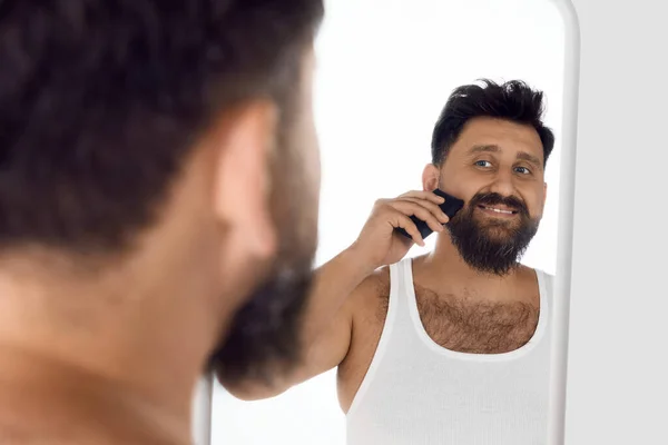 面带微笑的男人看着镜子 留著胡子 在白色的工作室背景上刮胡子 男性美感 皮肤护理 健康和健康的概念 广告的复制空间 — 图库照片